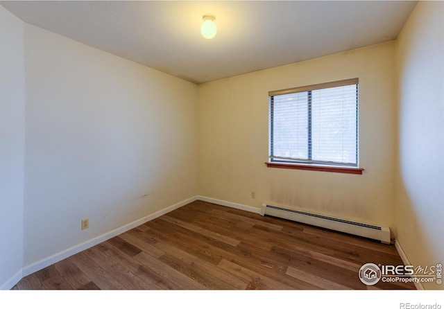 spare room featuring baseboards, a baseboard heating unit, and wood finished floors