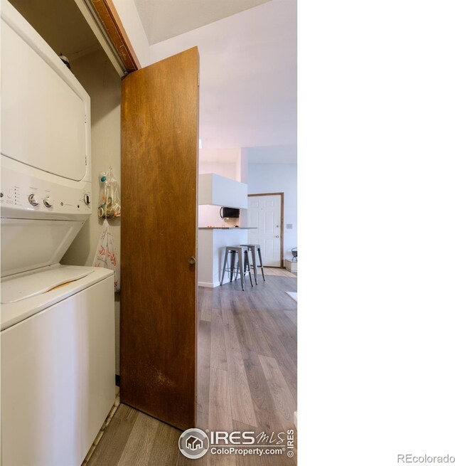 clothes washing area with stacked washer and dryer, laundry area, and wood finished floors