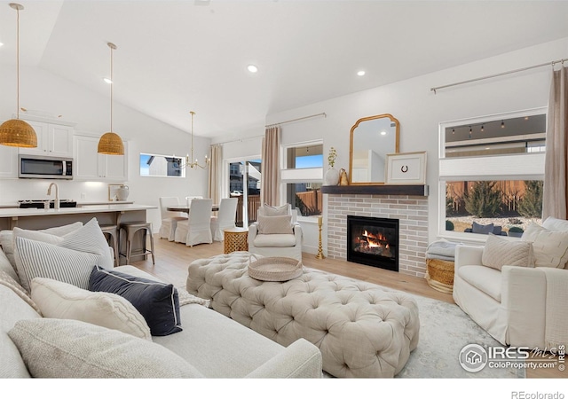 living room featuring high vaulted ceiling, recessed lighting, a brick fireplace, and light wood finished floors