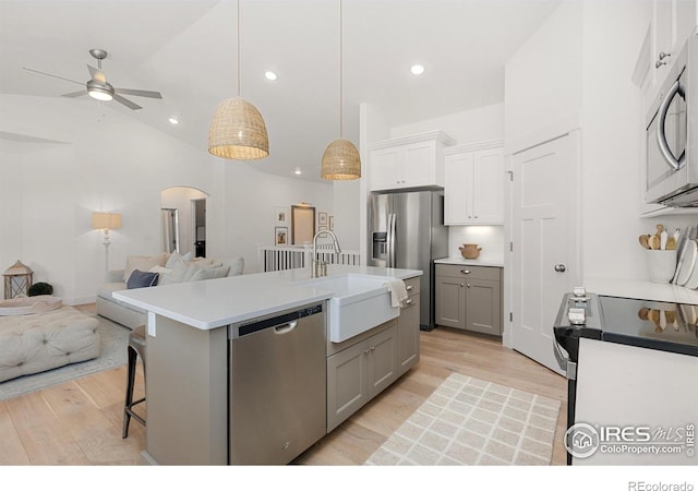 kitchen with arched walkways, open floor plan, stainless steel appliances, gray cabinetry, and a sink