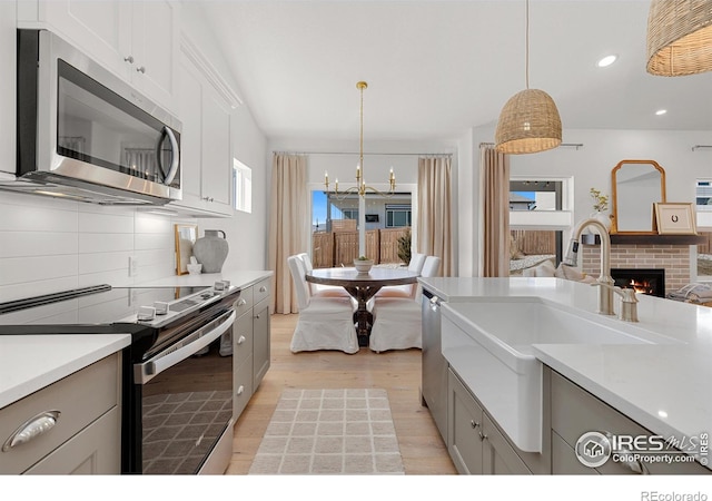 kitchen with light wood finished floors, tasteful backsplash, appliances with stainless steel finishes, a brick fireplace, and a sink