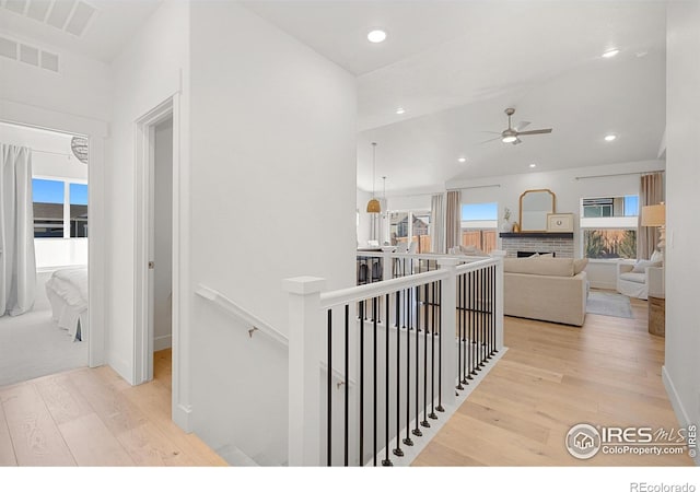 hallway with light wood-style floors, recessed lighting, and an upstairs landing