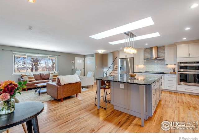 kitchen featuring decorative backsplash, a kitchen island, appliances with stainless steel finishes, open floor plan, and wall chimney range hood