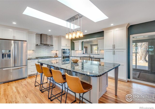 kitchen featuring stainless steel appliances, a skylight, a kitchen breakfast bar, wall chimney range hood, and a center island