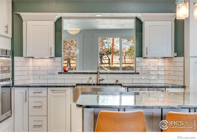 kitchen featuring backsplash, dark stone countertops, a sink, and white cabinets