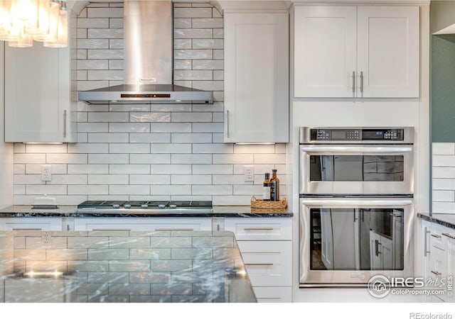 kitchen featuring stainless steel appliances, wall chimney range hood, decorative backsplash, and white cabinets