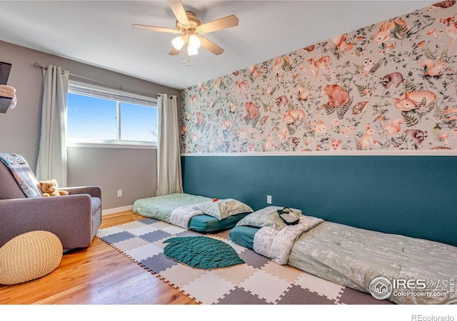 bedroom with wainscoting, ceiling fan, wood finished floors, baseboards, and wallpapered walls