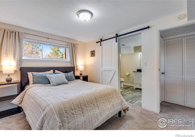 carpeted bedroom with ensuite bath, a barn door, baseboards, and a closet