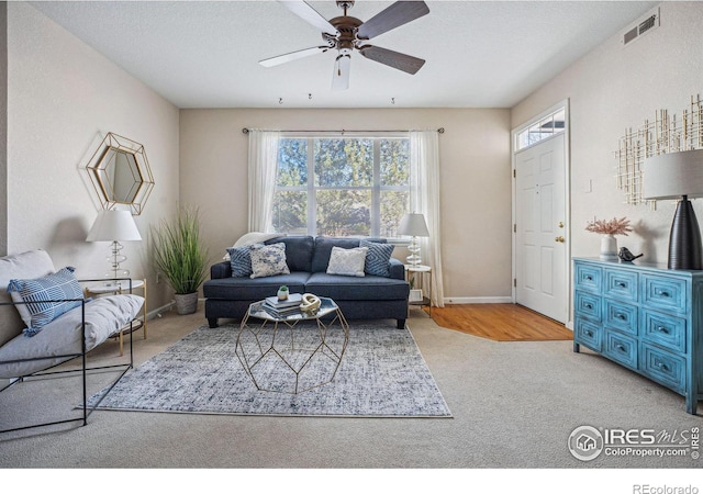 carpeted living room featuring a ceiling fan, visible vents, a textured ceiling, and baseboards