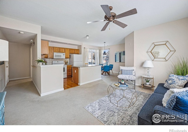 living room featuring light carpet, baseboards, and a ceiling fan