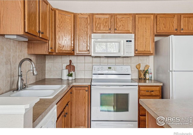 kitchen featuring white appliances, brown cabinetry, a sink, light countertops, and backsplash