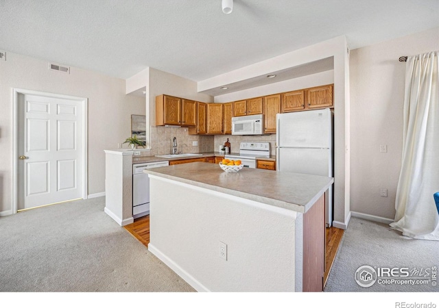 kitchen featuring white appliances, a kitchen island, a sink, visible vents, and light countertops