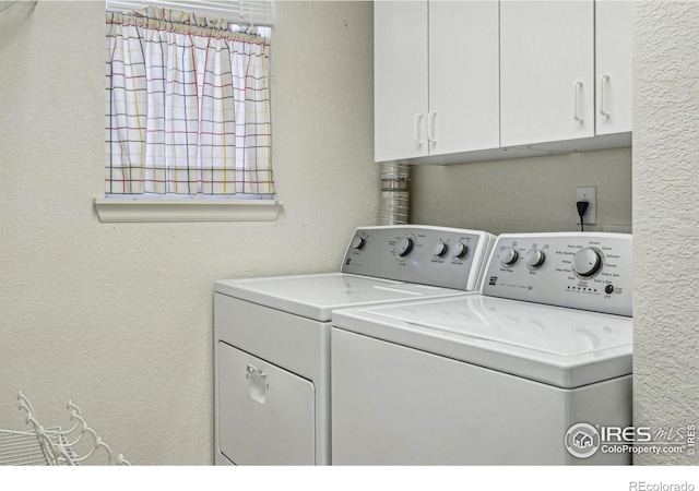 clothes washing area featuring a textured wall, separate washer and dryer, and cabinet space