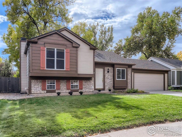 tri-level home featuring an attached garage, fence, concrete driveway, stone siding, and a front lawn