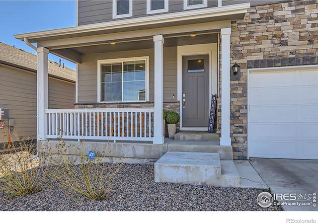 doorway to property with covered porch, stone siding, and an attached garage