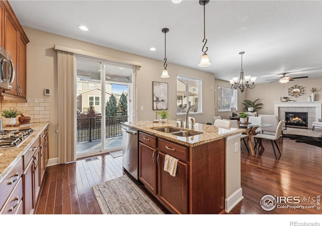 kitchen with a tiled fireplace, appliances with stainless steel finishes, dark wood-style flooring, hanging light fixtures, and a sink