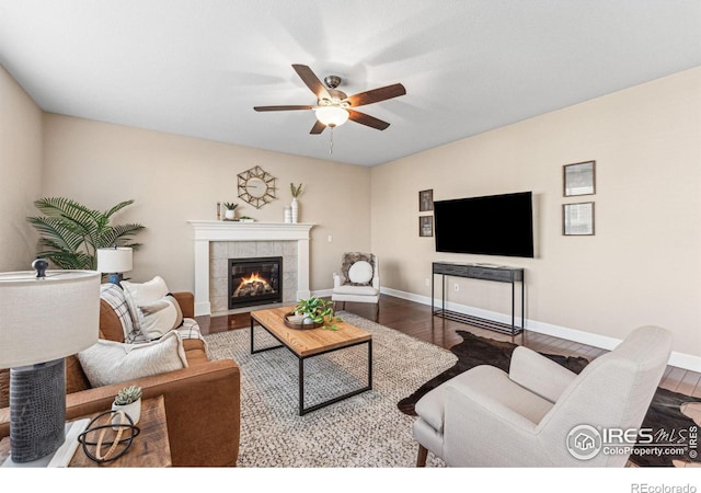 living area featuring a tile fireplace, wood finished floors, a ceiling fan, and baseboards