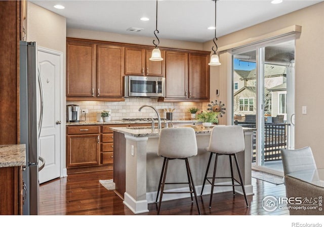 kitchen with dark wood-style floors, appliances with stainless steel finishes, backsplash, and brown cabinets