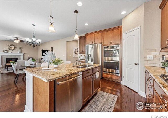 kitchen featuring stainless steel appliances, a sink, dark wood-style floors, tasteful backsplash, and a tiled fireplace