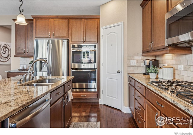 kitchen with stainless steel appliances, dark wood-type flooring, a sink, and light stone countertops