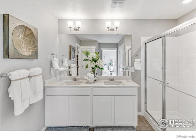 bathroom with a notable chandelier, a sink, a shower stall, and double vanity