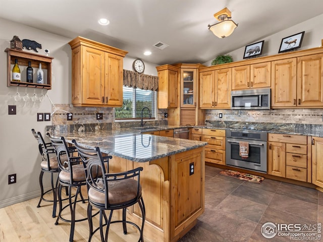 kitchen featuring decorative backsplash, glass insert cabinets, appliances with stainless steel finishes, a kitchen breakfast bar, and a sink