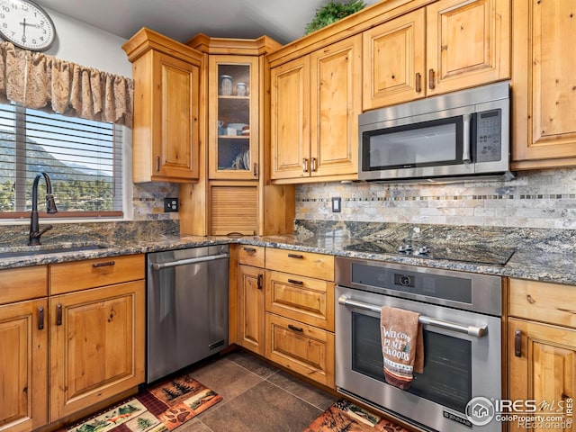 kitchen featuring appliances with stainless steel finishes, decorative backsplash, a sink, and dark stone counters