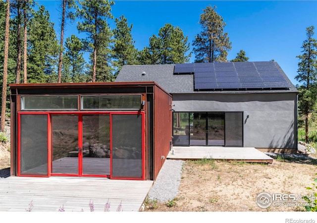 rear view of house featuring a deck, solar panels, and stucco siding