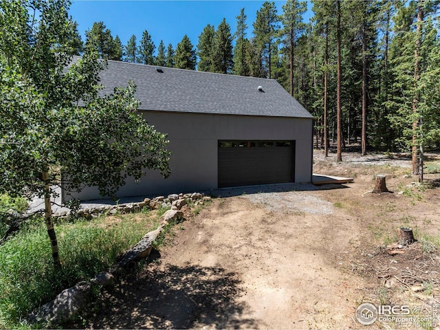 view of property exterior with dirt driveway and roof with shingles