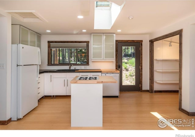 kitchen with white appliances, light wood finished floors, glass insert cabinets, a center island, and a sink