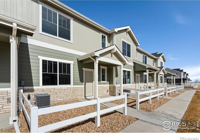 view of property featuring stone siding, a fenced front yard, and central AC unit