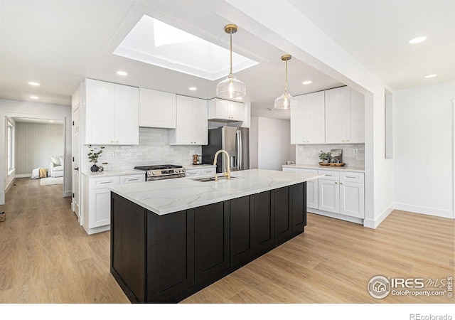 kitchen with stainless steel appliances, white cabinetry, light wood-style flooring, and light stone countertops