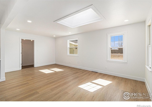 unfurnished room featuring baseboards, light wood finished floors, a skylight, and recessed lighting