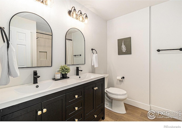 full bath featuring double vanity, wood finished floors, a sink, and toilet