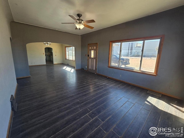 empty room featuring dark wood-type flooring, arched walkways, visible vents, and ceiling fan