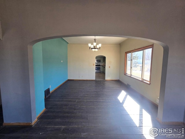 unfurnished room with baseboards, visible vents, arched walkways, and wood finished floors