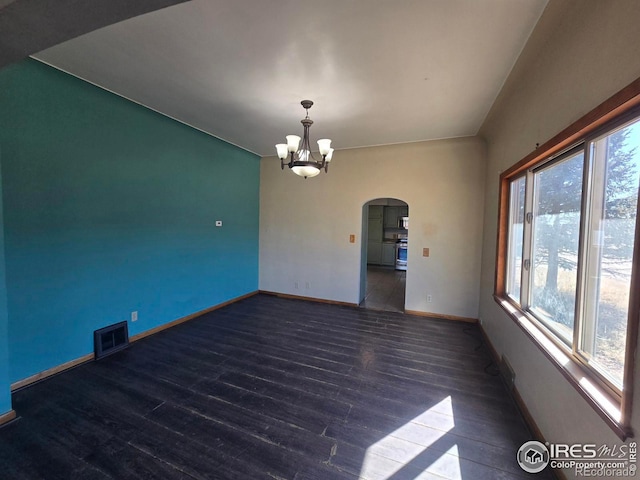 empty room featuring arched walkways, wood finished floors, visible vents, and a chandelier