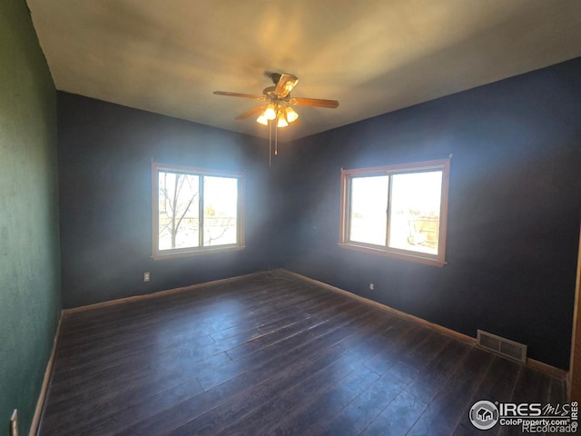 empty room featuring a wealth of natural light, wood-type flooring, visible vents, and ceiling fan