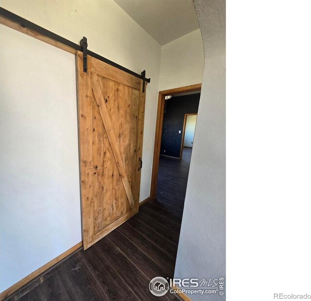 corridor featuring dark wood-style floors, arched walkways, baseboards, and a barn door