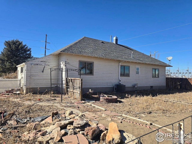 rear view of property featuring a shingled roof, central AC, and fence