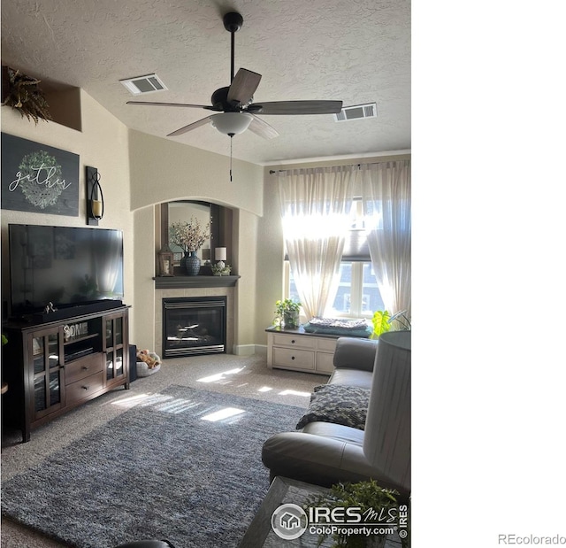 carpeted living room with visible vents, a textured ceiling, and a glass covered fireplace