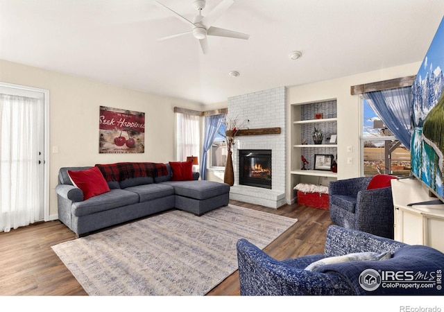 living room with ceiling fan, a fireplace, built in features, and wood finished floors