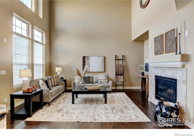 living area featuring a tile fireplace, a towering ceiling, baseboards, and wood finished floors