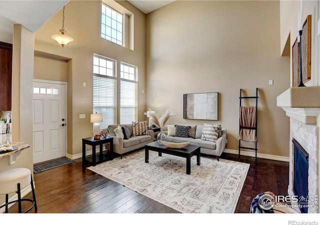 living area featuring a towering ceiling, a fireplace, baseboards, and dark wood finished floors