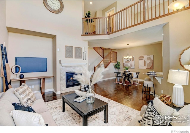 living room with a chandelier, a fireplace, wood finished floors, a towering ceiling, and baseboards