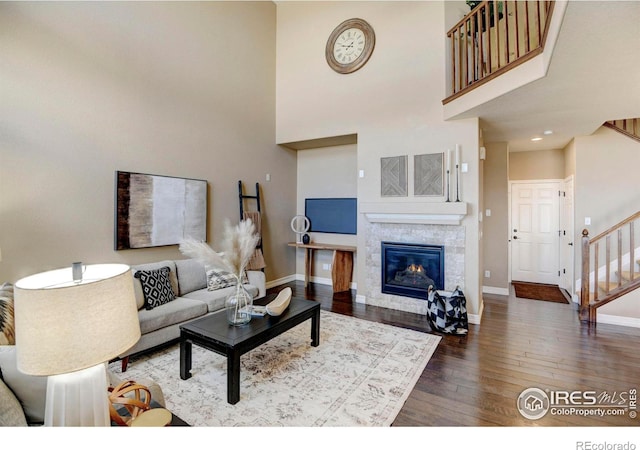 living area featuring a tile fireplace, a towering ceiling, baseboards, stairs, and hardwood / wood-style floors