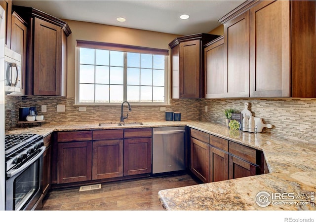 kitchen with light stone counters, stainless steel appliances, decorative backsplash, a sink, and wood finished floors