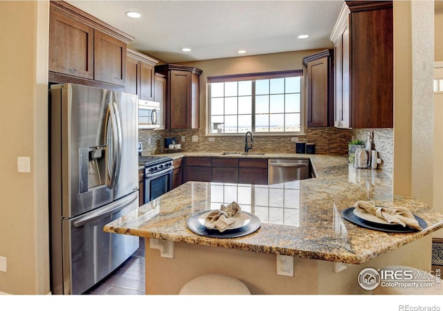 kitchen with light stone counters, stainless steel appliances, decorative backsplash, a sink, and a peninsula