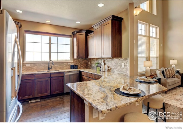 kitchen featuring dark wood finished floors, appliances with stainless steel finishes, a sink, a peninsula, and a kitchen breakfast bar