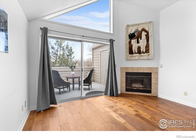 living area with vaulted ceiling, a tile fireplace, and wood finished floors